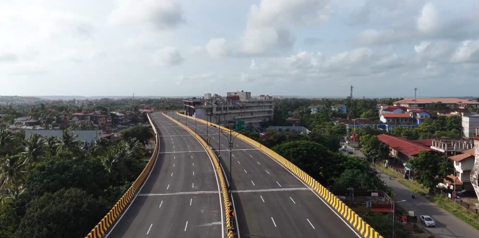 A close perspective view along the wide, six-lane asphalt surface of the Porvorim elevated corridor with yellow and black crash barriers.