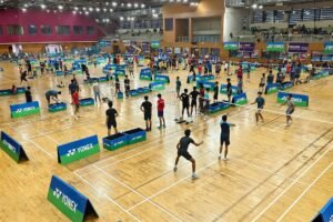 Elevated view of junior badminton players competing across multiple courts inside the Manohar Parrikar Indoor Stadium in Navelim, Goa.